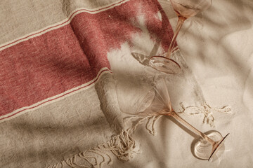 Striped linen beach towel with fringes, empty cocktail glasses  on sandy beach with shadows from...