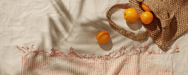 Fresh oranges falling out from woven bag on sandy beach. Linen beach towel with fringes detail. Tropical holidays concept - obrazy, fototapety, plakaty