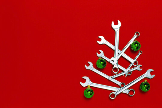 Christmas tree made of wrenches decorated with green balls on red background. New Year banner with tools. Postcard with place for greeting text. Happy new year. Industrial holiday concept. Copy space