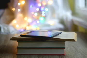 Stack of books, e-reader and colorful bokeh lights in the background. Selective focus.