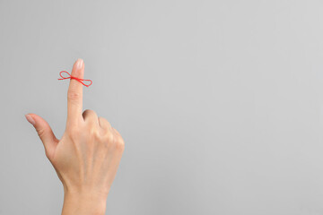 Woman showing index finger with tied red bow as reminder on light grey background, closeup. Space...