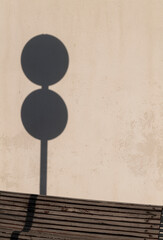 Shadow of street sign on white wall with wooden bench