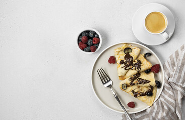 Breakfast with pancakes, berries and coffee on a white background with copy space. French crepes with chocolate, nuts and coffee on a white plate with copy space.