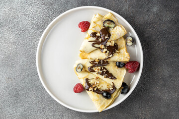Pancakes with chocolate and berries on a dark background, top view. The concept of the week of pancakes, Russian carnival. Russian pancakes.