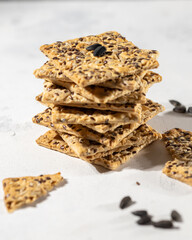 Stack of biscuit crackers with sunflowers seeds and sesame on white background, vertical, selective focus