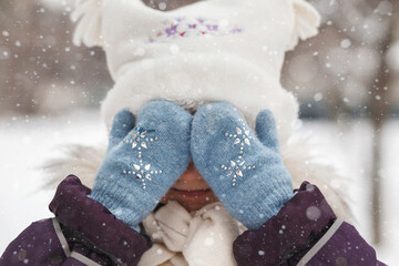 Face hands mittens eyes. Winter child face. Anticipation miracle. Hands in knitted mittens covering...