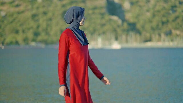 Young woman dressed in hijab mavo is walking by the sea. Young woman in stylish hijab swimsuit enjoying vacation alone.Slow motion video.