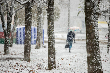 the city was covered by a snow storm, cold, climate change, movement is paralyzed because of the snow people move to the snowstorm on foot, hiding umbrellas and hoods, abnormal winter, precipitation