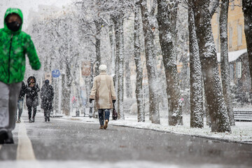 the city was covered by a snow storm, cold, climate change, movement is paralyzed because of the snow people move to the snowstorm on foot, hiding umbrellas and hoods, abnormal winter, precipitation