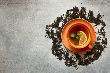Orange ceramic cup of tea with mint leaf and lemon slice on gray concrete background with copy space, top view