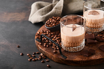 Glass of Irish cream baileys liqueur with roasted coffee beans, cinnamon and chocolate on dark wood background table. Selective focus.