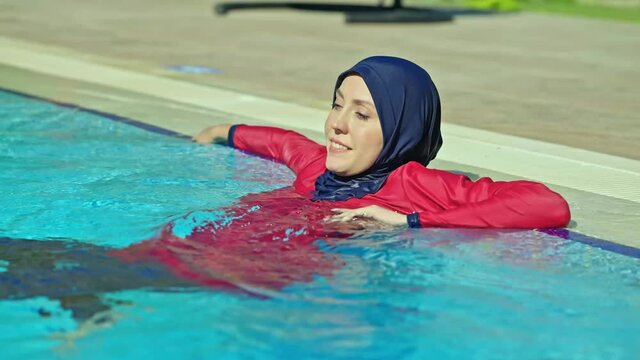 Young woman in a hijab swimsuit, cooling off by swimming in the pool, is enjoying her vacation. Slow motion video.Young woman wearing hijab swimsuit enjoying vacation.