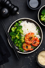 Teriyaki shrimps, rice and broccoli on a black plate. Asian healthy food. Seafood with garnish.  Top view