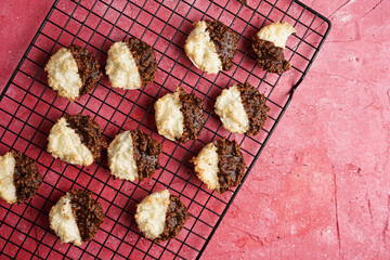 Several coconut flakes cookies dipped in chocolate on a baking rack on magenta surface, top view