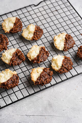 Several coconut flakes cookies dipped in chocolate on a baking rack on grey concrete surface, top view