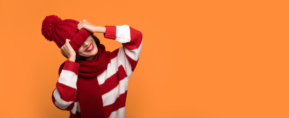 Banner photo of Excited funny young smiling girl is covering her face with help of big red winter hat while posing on yellow background