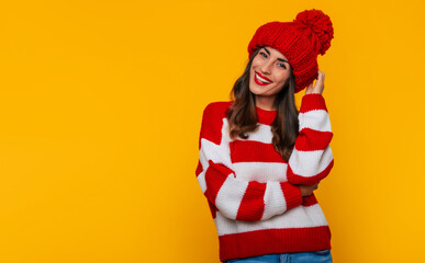 Close up photo of a beautiful happy brunette woman in red winter hat and scarf and posing isolated on yellow background