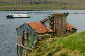 Europe, Faroe Islands. View of abandoned fishing shed with a salmon farm in the background.