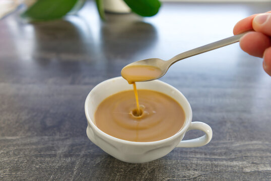 Coffee with milk in a white mug. The hand stirs the cofee with a spoon. A drop of coffee falls into a mug. close up