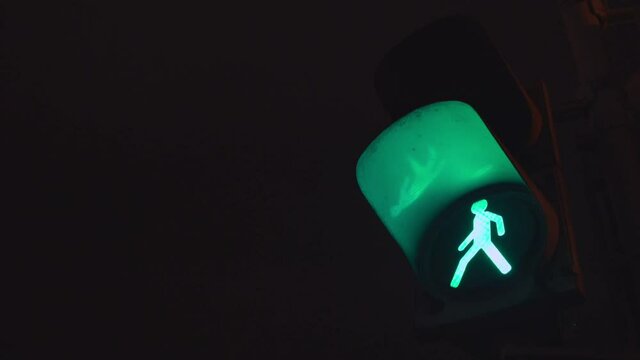 Pedestrian stoplight hanging on pole near street junction for people safety. Green and red signal is changing at night.