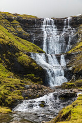 Obraz premium Europe, Faroe Islands. View of waterfall cascading down a hillside in the Faroe Islands.