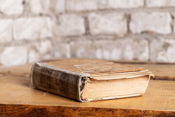 An old book in a battered binding lies against a brick wall made of light brick. Close-up, selective focus