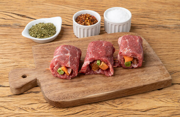 Rolled beef or roulade, vegetable and bacon stuffed meat over wooden table with seasonings