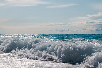 Shining on sun waves splash with white foam on sea coast. Blue epic seascape on Lefkada island in Greece. Summer travel to Ionian Sea