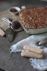 Tiramisu cake in a crystal square large plate on the table with a spruce towel and spoons. Dessert with mascarpone and savoyardi cookies.