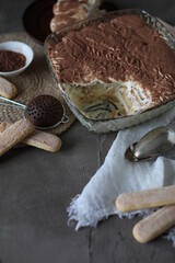 Tiramisu cake in a crystal square large plate on the table with a spruce towel and spoons. Dessert with mascarpone and savoyardi cookies.