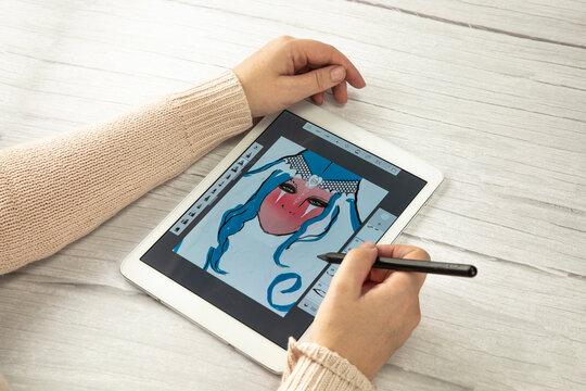 Young creative designer holding stylus pen drawing on screen of digital tablet on wooden desk with copy space, modern digital art top view