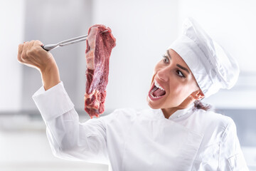 Female chef in rondon pretends wanting to bite into a raw cut of red meat she holds on a fork