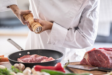 Professional chef grinds pepper on a raw piece of red meat in a pan