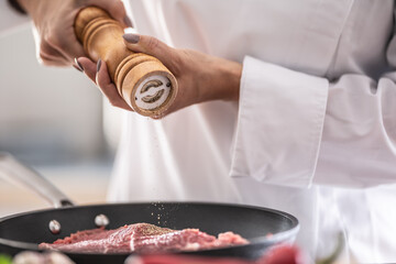 Detail of a wooden pepper grinder putting spice on cut of pork in a pan