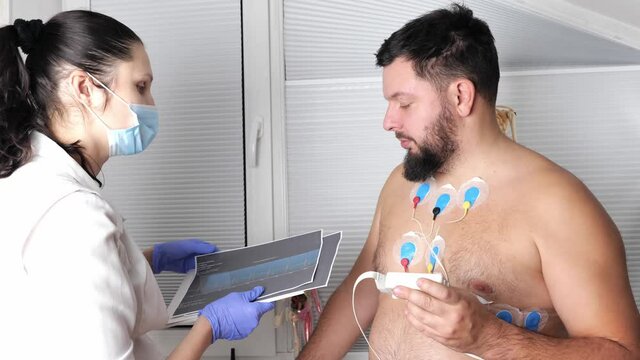 man patient with ECG cardiogram of heart, doctor cardiologist attaches sensors, examining and monitoring using holter equipment device for 24 hours daily monitoring of electrocardiogram, recorder