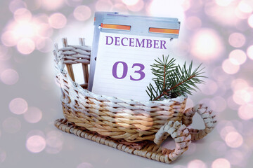Calendar for December 3: leaves of a calendar with the name of the month, numbers 0 and 3 in a decorative sleigh, a spruce branch on a light background, close-up, bokeh