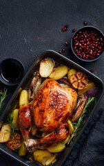 Festive roasted chicken in pomegranate sauce with potatoes in a gray ceramic mold. Dark background....