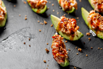 Sliced avocado seasoned with sauce lies on a dark background. Selective focus.