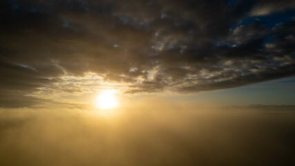 Aerial View. Flying in fog, fly in mist over the early morning clouds in the rising sun. Aerial camera shot. Flight above the clouds towards the sun with the mist clouds floating by. Misty weather