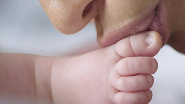  Video of mother kissing her son’s feet. Close up shot of a loving mother’s kiss. Macro cinematic footage shot: Mom kissing baby's fingers on leg. .Mum cares of her infant baby.