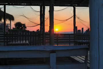 Orange sunrise on the beach with bungalows and fishing net