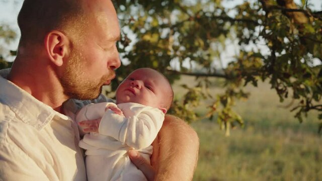 Happy smiling  dad is looking on her newborn baby.  Infant  is  in  father's arms, outdoors while sunset.   Father with newborn son. Happiness: daddy and child. Concept of happy  parenthood.
