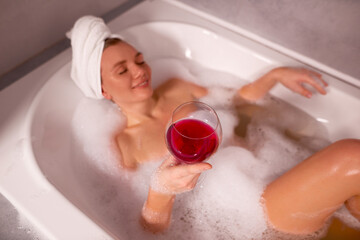woman drink wine in bathtub with foam. woman with towel on head lies in bath and relax. shallow...