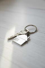 Silver key with silver house figure on white wooden background, buying new house real estate concept copy space