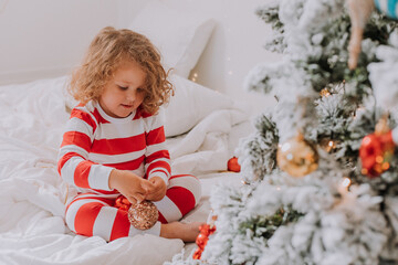 little girl in Christmas striped pajamas decorates the Christmas tree. lifestyle. High quality photo