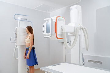 Side view of pretty brunette turned at side scanning chest and stomach in cabinet of radiology....