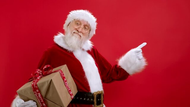 Santa Claus With Gift Box Pointing to CopySpace, Showing Layout of Workspace Mockup for Advertising, an Empty Space for Text or Image, Advertising Content on Red Background. Discount, Black Friday.