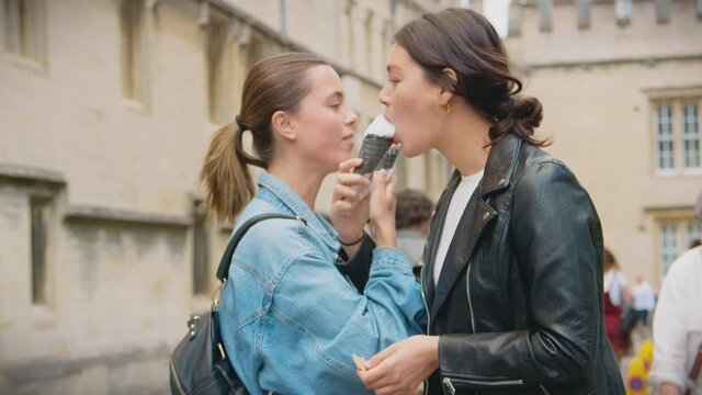 Happy same sex female couple sightseeing and eating ice cream cones as they walk around Oxford UK together - shot in slow motion