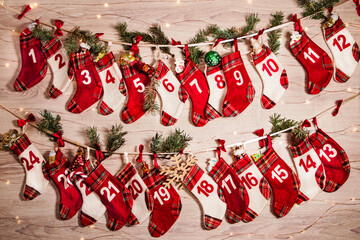 Advent calendar with gifts in children's socks, branches of a Christmas tree, lights of garlands on a wooden background. 24 socks of the Advent calendar hang on the wall in anticipation of the holiday