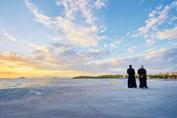 Two priests walking on the sea promenade with wonderful sunset view.